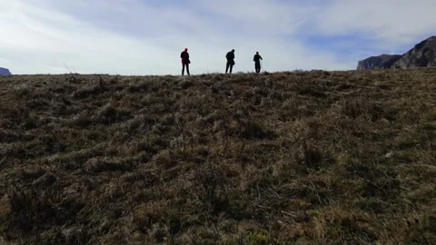 Three people walk down a dangerous slope in the mountains, shooting from a drone Stock Footage 171294381