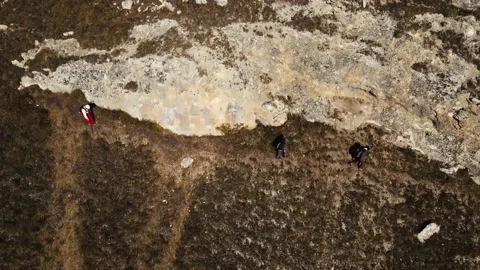 Three people walk down a dangerous slope in the mountains, shooting from a drone Stock Footage 171294704