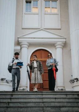 Three people walking down steps in front of classical building with columns Fotos de archivo