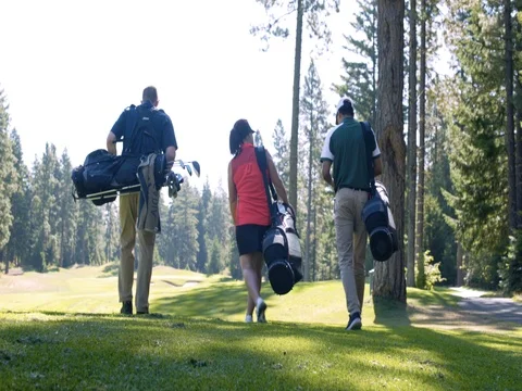 Three people walking on a golf course with sporting equipment Video stock 76236423