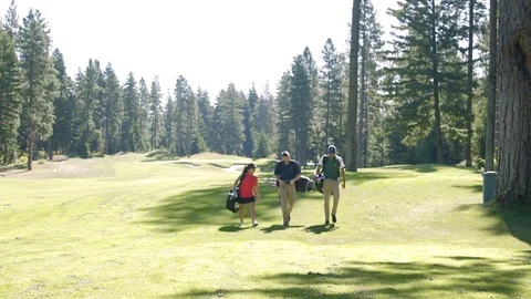 Three people walking on a golf course with sporting equipment Stock-Footage 76236446