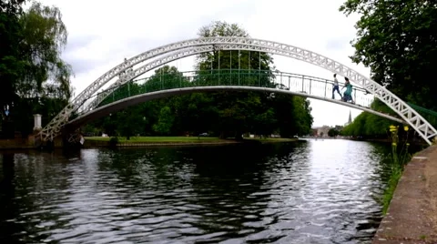Three People walking over a arched foot bridge to cross a river Stock Footage 45604047