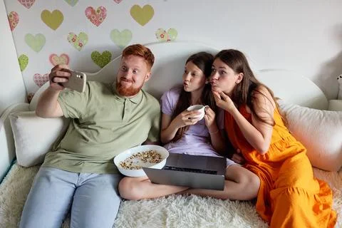 Three people on a white couch taking a selfie: left person holds phone and .. Fotos de archivo