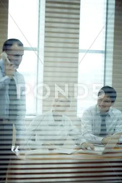 Three people working in office viewed through jalousie Stock Photos