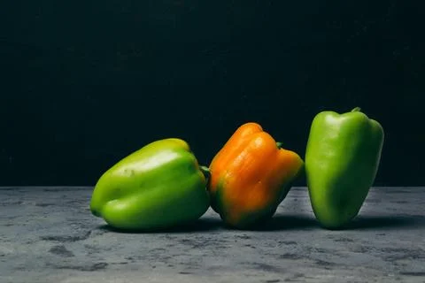 Three peppers are on a table, one green and two orange Stock Photos
