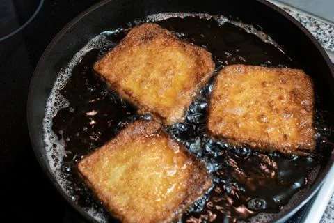 Three pieces of eggy bread cooking in hot oil in a pan close up shot Stock Photos