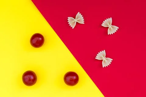 Three pieces of farfalle paste and three cherry tomatoes on a contrasting bac Stock Photos