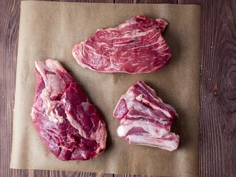 Three pieces of fresh raw beef are spread out on parchment. Top view, flat la Stock Photos