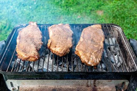 Three pieces of marinated flat iron steak on a charcoal grill Stock Photos