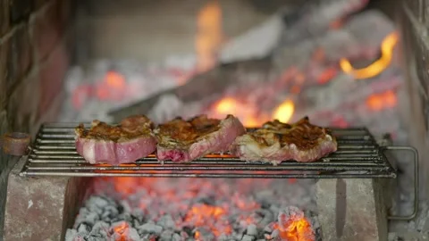 Three pieces of meat grilling over coals in stone fireplace 2026 Stock Footage 332197666