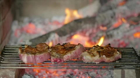 Three pieces of meat grilling over coals in stone fireplace Video stock 332197671