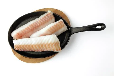 Three pieces of raw cod fillet on a black cast iron frying pan prepared for.. Stock Photos