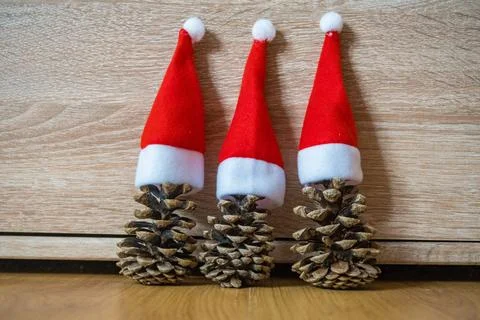 Three pine cones in a red Santa hats like a Christmas tree on wooden background Stock Photos