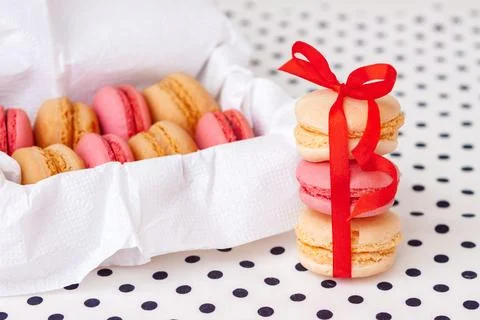 Three pink and beige macarons tied with a vibrant red ribbon beside an open.. Stock Photos
