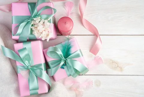 Three pink gift boxes, a candle and ribbons on a white wooden background. Stock Photos