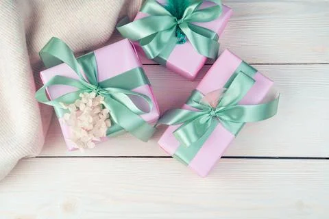 Three pink gift boxes with ribbons and a sweater on a white wooden background. Stock Photos