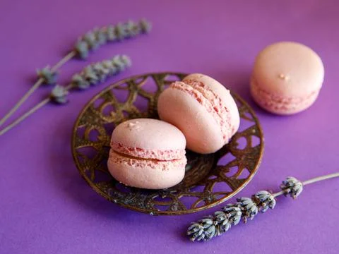 Three pink macaroons close-up on bright purple background with lavender flowe Stock Photos