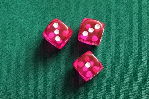 Three pink translucent dice with white dots on green felt table, gambling and Stock Photos