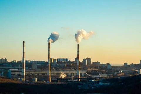 Three pipes from the CHP stand in the background of the city. The pipes release Stock Photos