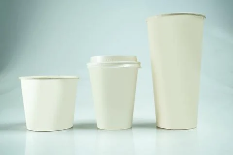 Three plain white paper cups of different sizes arranged in a row against a.. Stock Photos