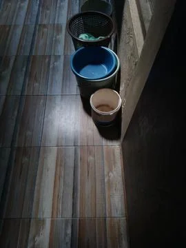 Three plastic buckets sit on a tiled wall floor with a wooden look, set again Stock Photos