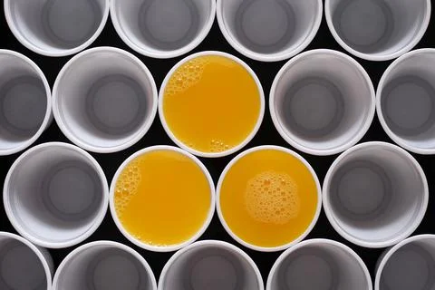 Three plastic disposable cups filled with orange juice, among many other cups Stock Photos