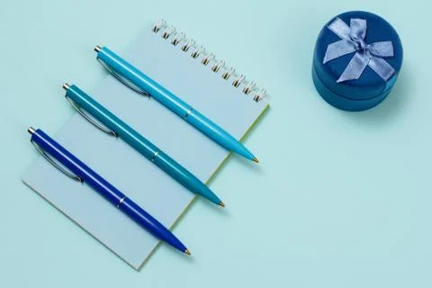 Three plastic pens and notebook on a blue background. Stock Photos