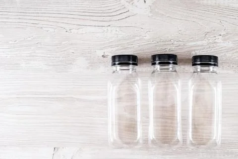 Three plastic transparent empty bottles with a black cap on a wooden table Stock Photos