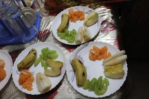 Three plates each hold sliced banana, green grapes, mandarin orange sections, Stock Photos
