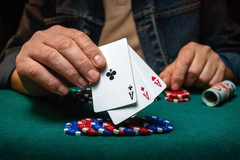 Three playing cards with aces are held above stacks of colorful poker chips.. Foto stock