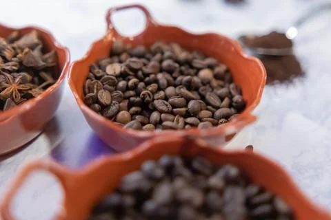 Three pots of roasted coffee beans and star anise seeds on white surface Foto stock