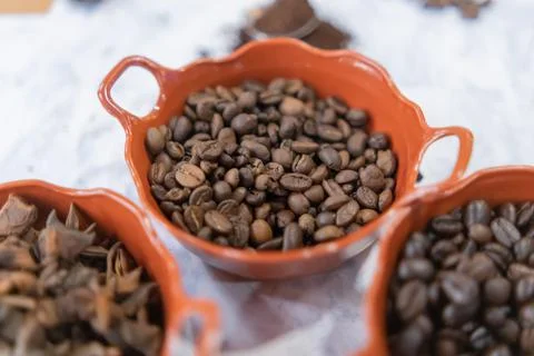 Three pots of roasted coffee beans and star anise seeds on white surface Stock Photos