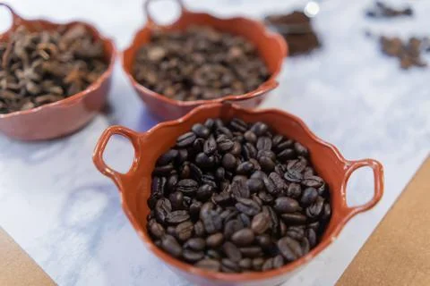 Three pots of roasted coffee beans and star anise seeds on white surface 스톡 사진