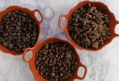 Three pots of roasted coffee beans and star anise seeds on white surface Stock Photos