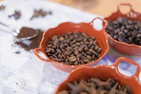 Three pots of roasted coffee beans and star anise seeds on white surface Stock Photos