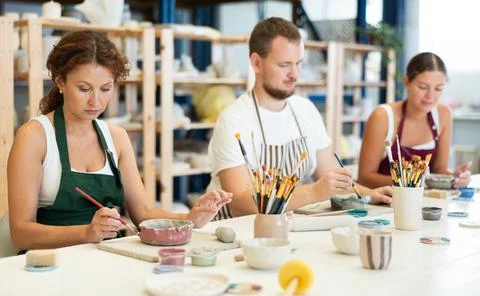 Three pottery masters work together on ceramic tableware, enjoying creative Stock Photos