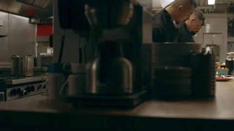 Three professional chefs cutting vegetables for cooking at a long counter in ind Stock Footage 199460407