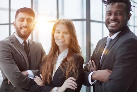 Three professionals in formal suits standing for camera indoors and smiling Stock Photos