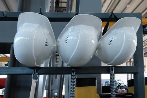 Three protective white helmets hang on the rack in the factory. The concept o Stock Photos