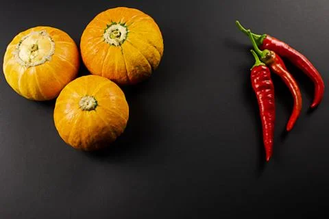 Three pumpkins, capsicum on a black background Stock Photos