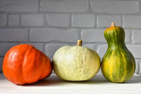 Three pumpkins orange, white and green pumpkins on a wooden table against a Stock Photos