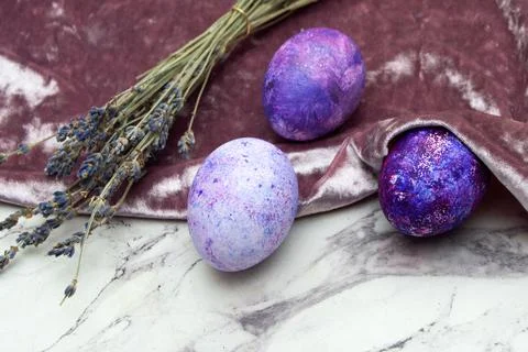 Three purple eggs are lying, covered with a velvet cloth on a marble background  Stock Photos