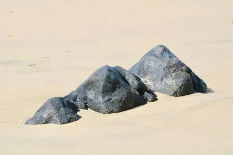 Three pyramid shaped rocks surrounded by sand on a sunny day Stock Photos