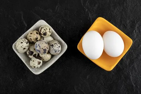 Three quail eggs and chicken eggs on black background Stock Photos