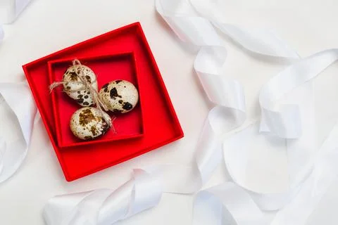 Three quail eggs in a red box on a background of white ribbons Stock Photos