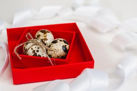 Three quail eggs in a red box on a background of white ribbons Stock Photos