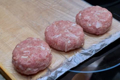Three raw meat cutlets lie on a wooden plank ready to be cooked. Stock Photos