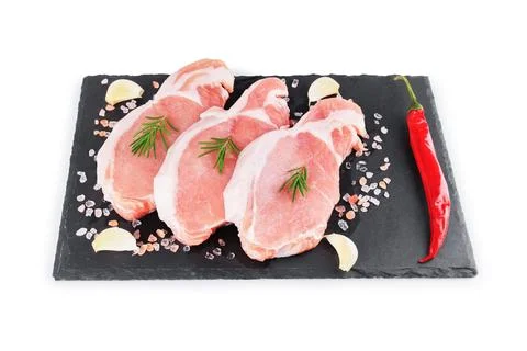 Three raw pork chops on a black slate board with rosemary, garlic, chili pe.. Stock Photos