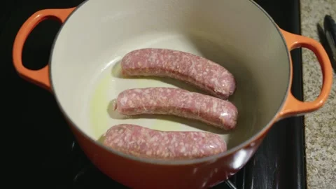 Three Raw Sausages Searing in Hot Oil in a Bright Orange Dutch Oven Stock Footage 317874853