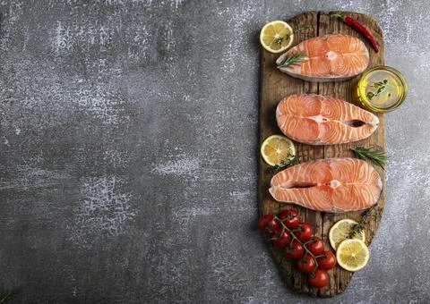 Three raw steak fish trout, salmon and spices on wooden board, dark background Stock Photos
